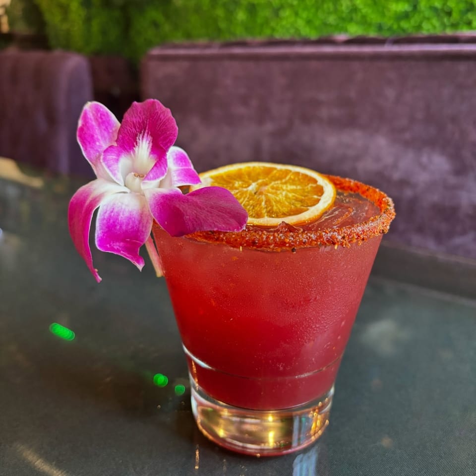 A vibrant red margarita with a chili-lime rim, orange slice, and pink orchid garnish.