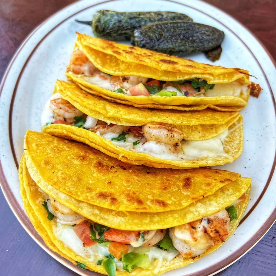 Four shrimp tacos with melted cheese, diced tomatoes, and cilantro, served with two grilled jalapeños.